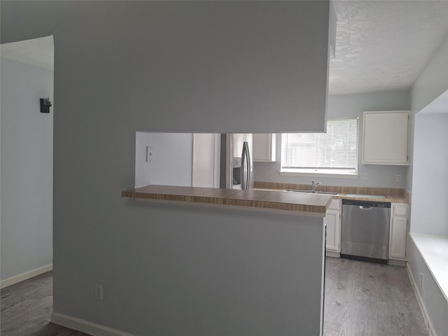 kitchen featuring stainless steel dishwasher, a sink, light wood-style floors, and white cabinetry