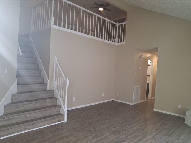 staircase featuring baseboards, wood finished floors, a towering ceiling, and visible vents