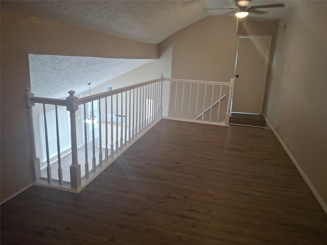 hall featuring lofted ceiling, wood finished floors, an upstairs landing, baseboards, and a textured ceiling
