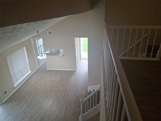 stairs featuring baseboards, visible vents, a notable chandelier, lofted ceiling, and wood finished floors