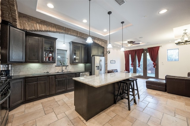 kitchen with a kitchen island, decorative light fixtures, stainless steel appliances, ceiling fan, and a tray ceiling