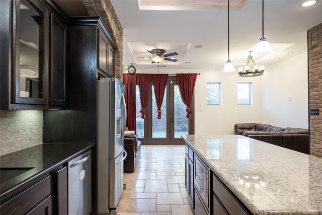 kitchen featuring light stone countertops, appliances with stainless steel finishes, a raised ceiling, pendant lighting, and ceiling fan with notable chandelier