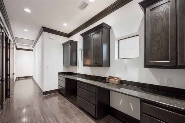 kitchen with crown molding, dark brown cabinets, dark hardwood / wood-style floors, dark stone countertops, and built in desk