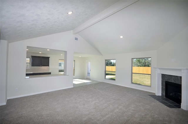 unfurnished living room with a tile fireplace, a textured ceiling, vaulted ceiling with beams, and dark carpet