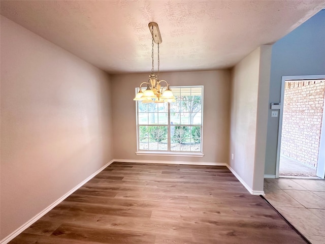 unfurnished dining area featuring an inviting chandelier, a textured ceiling, and dark hardwood / wood-style floors