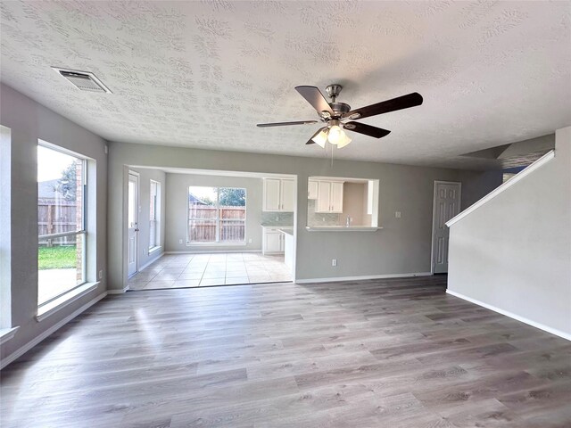 unfurnished living room with ceiling fan, light wood-type flooring, and a textured ceiling