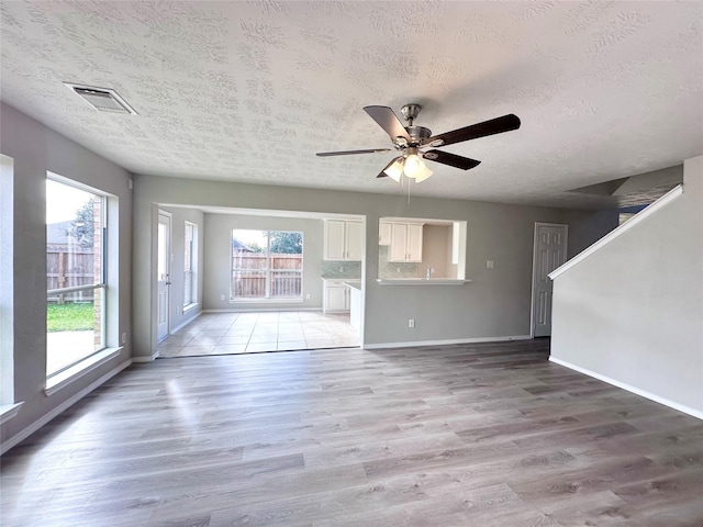 unfurnished living room featuring ceiling fan, a healthy amount of sunlight, light hardwood / wood-style floors, and a textured ceiling