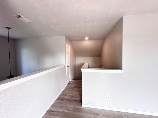 hallway with hardwood / wood-style flooring, a textured ceiling, and vaulted ceiling