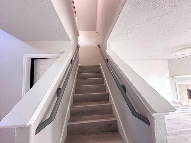 staircase with a tile fireplace and a textured ceiling