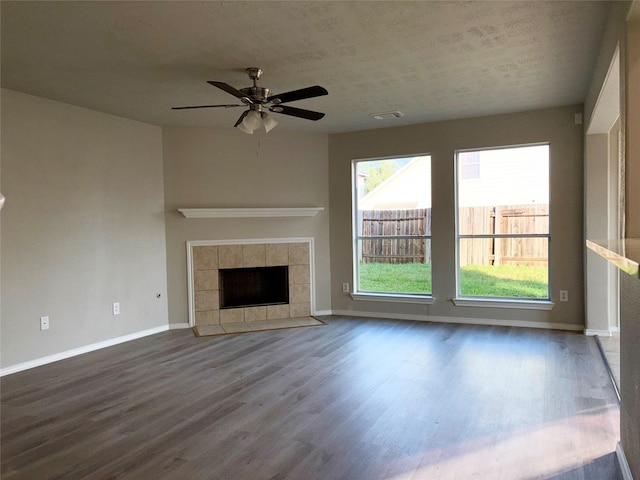 unfurnished living room with ceiling fan, dark hardwood / wood-style floors, a tile fireplace, and a textured ceiling