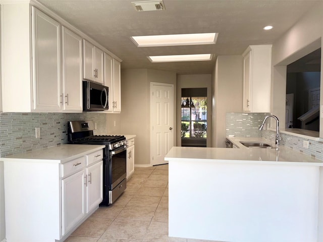 kitchen featuring kitchen peninsula, stainless steel appliances, light tile patterned floors, white cabinetry, and sink