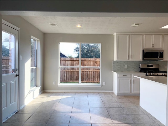 kitchen with white cabinets, stainless steel appliances, a wealth of natural light, and light tile patterned floors