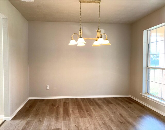 empty room featuring wood-type flooring and a notable chandelier