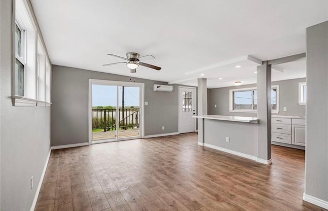 unfurnished living room with an AC wall unit, ceiling fan, and hardwood / wood-style floors