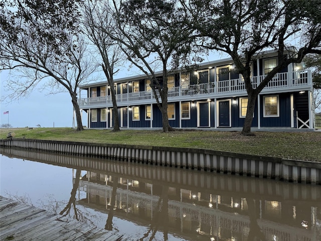 back of property with a water view, a yard, and a balcony