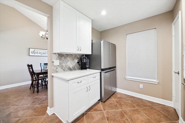 kitchen featuring vaulted ceiling, tile patterned flooring, decorative backsplash, white cabinetry, and stainless steel refrigerator