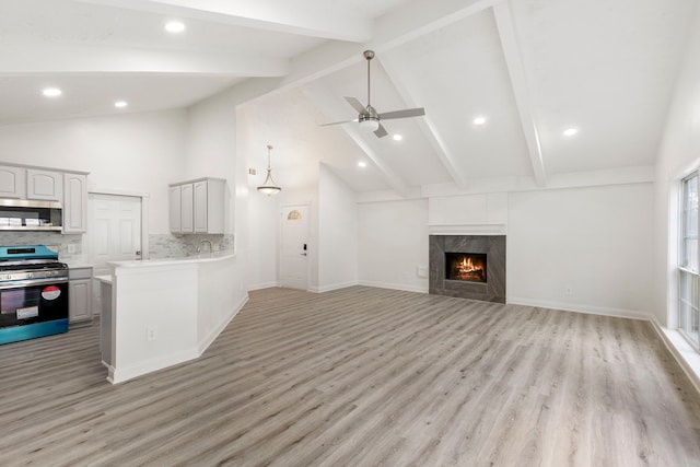 unfurnished living room with ceiling fan, beam ceiling, high vaulted ceiling, light hardwood / wood-style flooring, and a fireplace