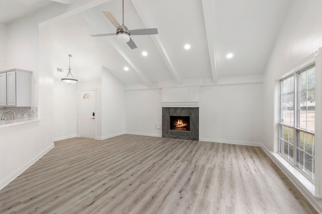 unfurnished living room featuring high vaulted ceiling, ceiling fan, light wood-type flooring, a fireplace, and beam ceiling