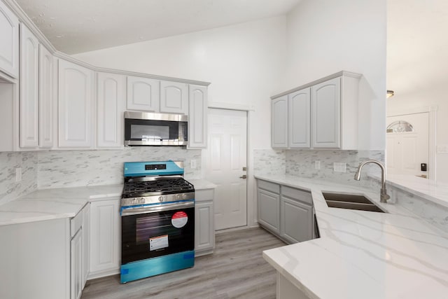 kitchen featuring white cabinets, stainless steel appliances, light stone counters, and sink