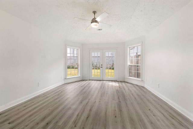 empty room featuring french doors, a wealth of natural light, a textured ceiling, ceiling fan, and light hardwood / wood-style flooring