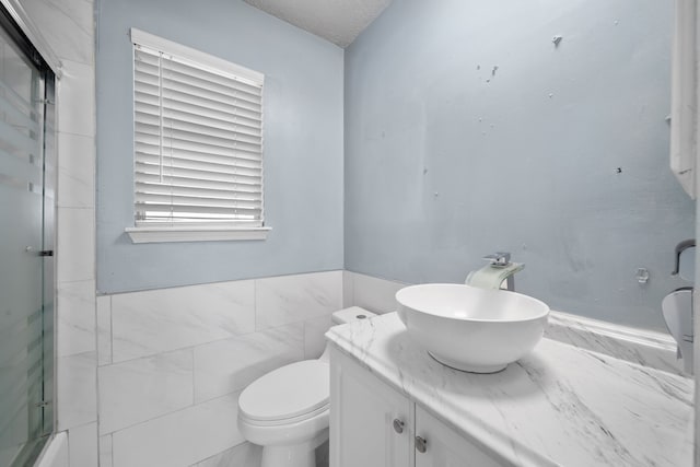 bathroom featuring vanity, toilet, tile walls, plenty of natural light, and a shower with shower door