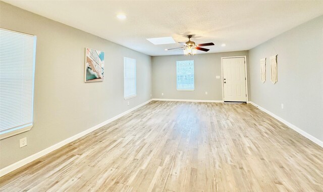 unfurnished room featuring ceiling fan, a textured ceiling, a skylight, and light hardwood / wood-style floors