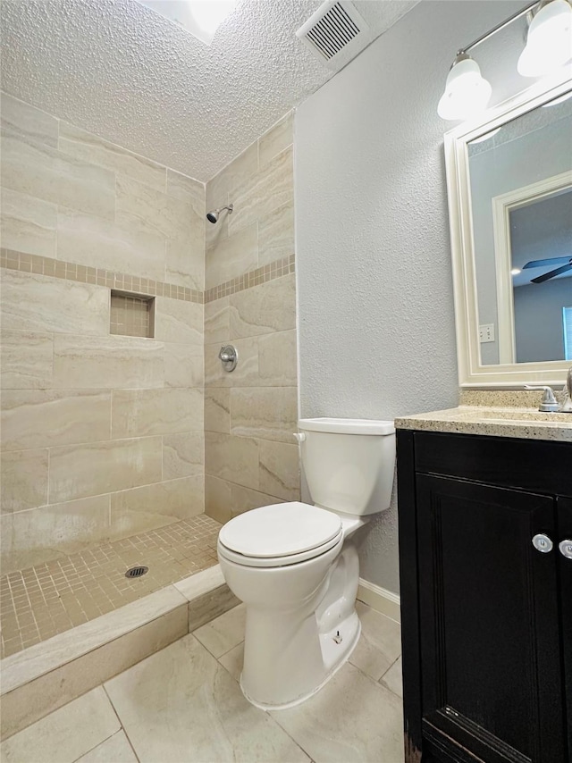 bathroom featuring toilet, a textured ceiling, a tile shower, tile patterned floors, and vanity