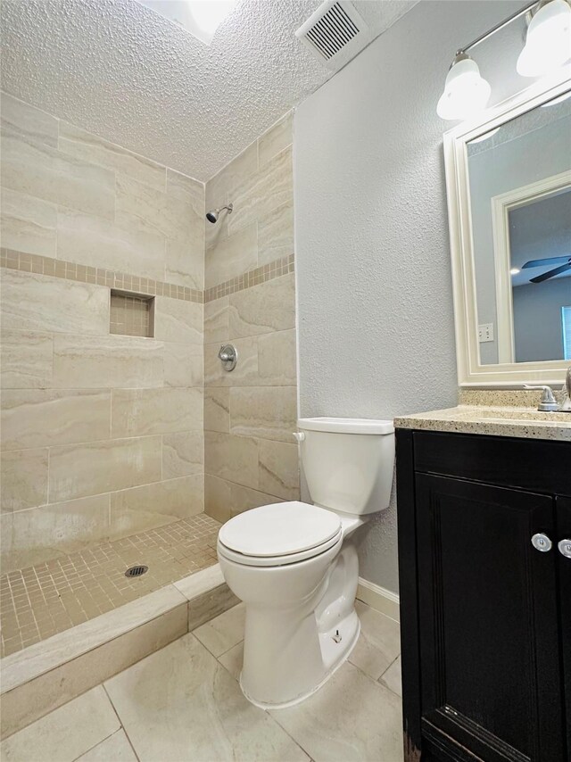 bathroom with tiled shower, vanity, a textured ceiling, tile patterned floors, and toilet