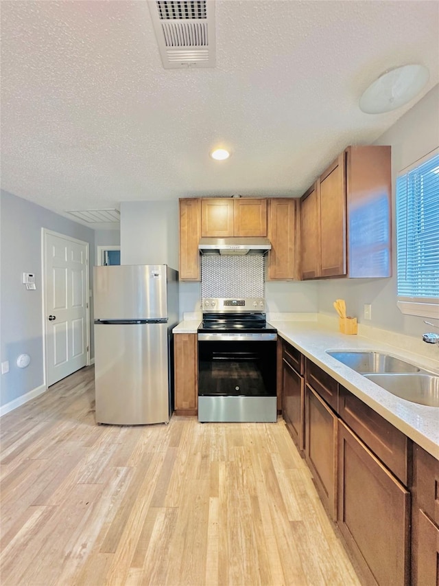 kitchen featuring appliances with stainless steel finishes, light wood-type flooring, sink, a textured ceiling, and tasteful backsplash