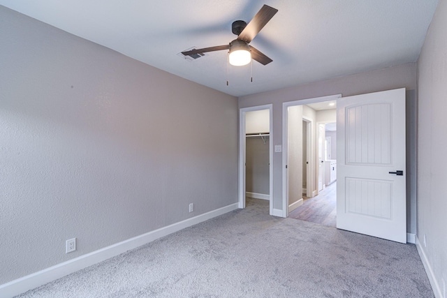 unfurnished bedroom with ceiling fan, a walk in closet, a closet, and light carpet