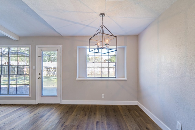 unfurnished dining area with dark wood-type flooring, a textured ceiling, beam ceiling, and an inviting chandelier