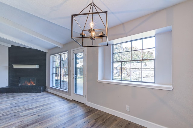 unfurnished living room with wood-type flooring, a wealth of natural light, lofted ceiling with beams, and a fireplace