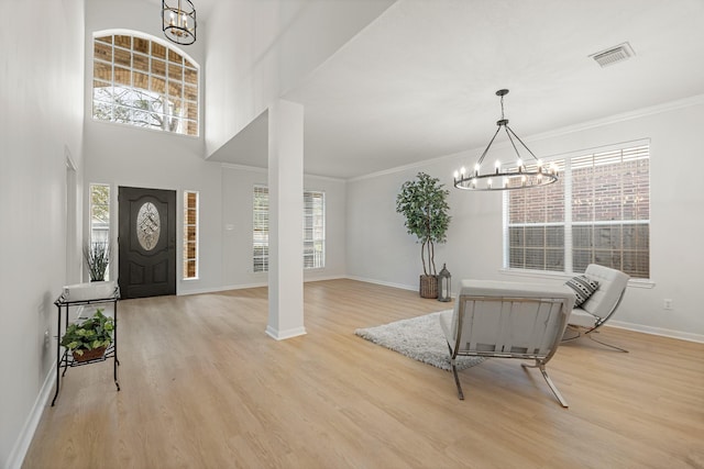 foyer entrance with light hardwood / wood-style floors, an inviting chandelier, plenty of natural light, and ornamental molding