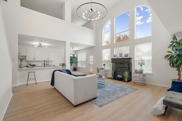 living room featuring a notable chandelier, light hardwood / wood-style floors, a premium fireplace, and a high ceiling