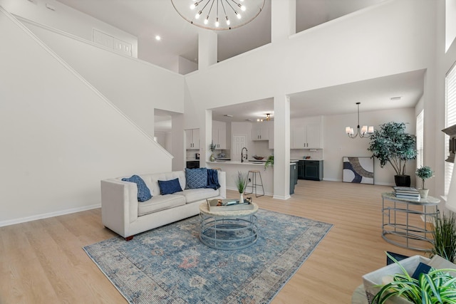 living room with sink, light hardwood / wood-style flooring, a high ceiling, and an inviting chandelier