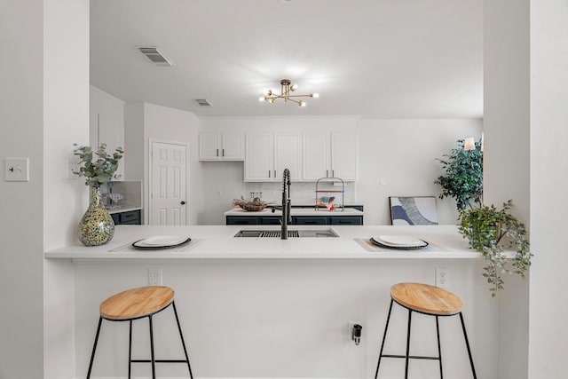 kitchen featuring white cabinetry, sink, kitchen peninsula, a chandelier, and a breakfast bar