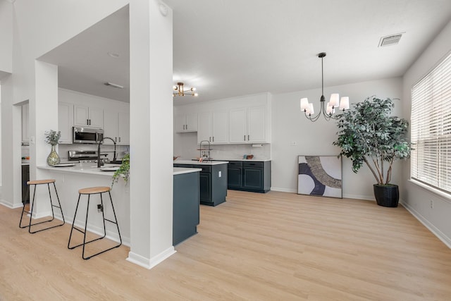 kitchen with appliances with stainless steel finishes, an inviting chandelier, white cabinetry, and decorative light fixtures