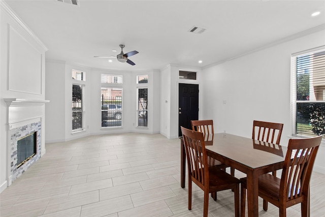 dining space with a tile fireplace, ceiling fan, and ornamental molding