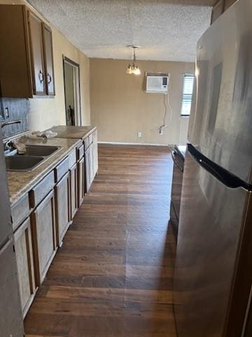 kitchen featuring dark wood-type flooring, sink, hanging light fixtures, stainless steel fridge, and a textured ceiling