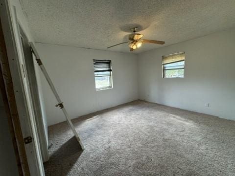 carpeted empty room featuring ceiling fan, a healthy amount of sunlight, and a textured ceiling