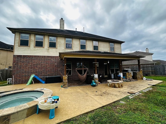 rear view of property featuring an outdoor hot tub, a patio, and a fire pit