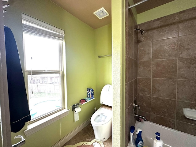 bathroom featuring tiled shower / bath combo, toilet, and a healthy amount of sunlight