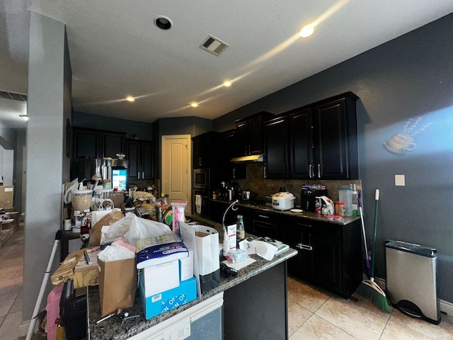 kitchen featuring decorative backsplash, light tile patterned floors, dark stone countertops, oven, and stainless steel microwave