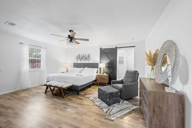 bedroom with a barn door, ceiling fan, and light hardwood / wood-style flooring