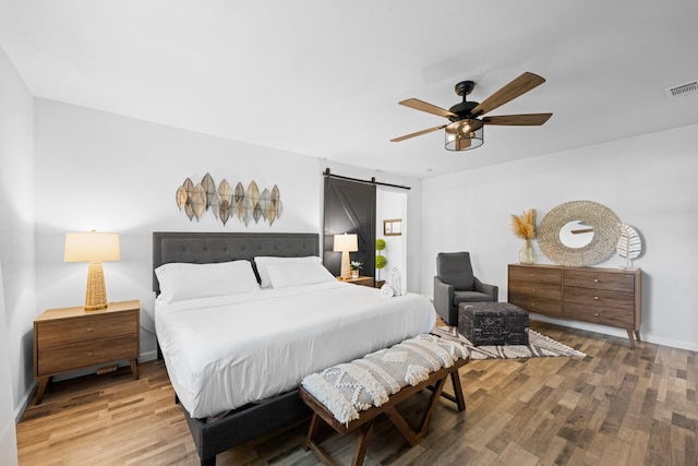 bedroom featuring wood-type flooring, a barn door, and ceiling fan