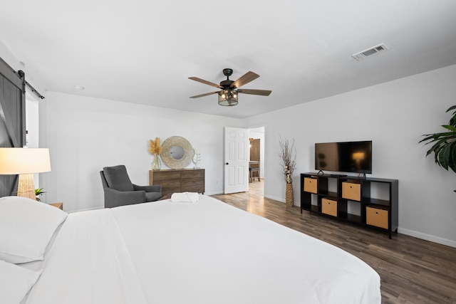 bedroom featuring ceiling fan, a barn door, and dark hardwood / wood-style flooring