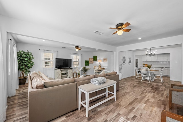 living room featuring ceiling fan with notable chandelier and light hardwood / wood-style floors