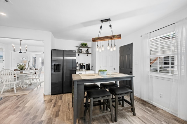 kitchen with pendant lighting, a breakfast bar, light wood-type flooring, a notable chandelier, and stainless steel fridge with ice dispenser