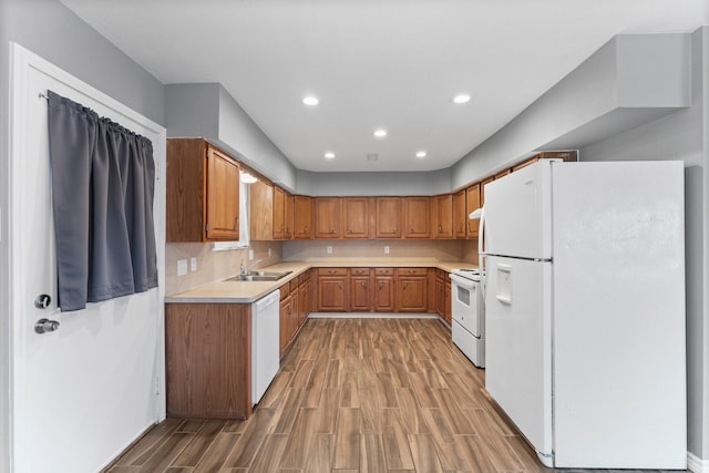 kitchen featuring wood-type flooring, sink, backsplash, and white appliances