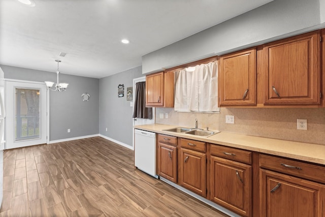 kitchen featuring sink, hanging light fixtures, backsplash, white dishwasher, and a notable chandelier